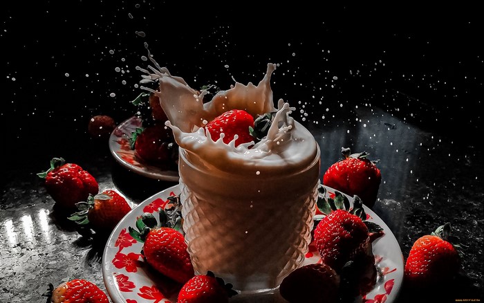 Strawberries splashing into milk in a glass