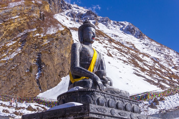 Buddha statue in snowy mountains with prayer flags