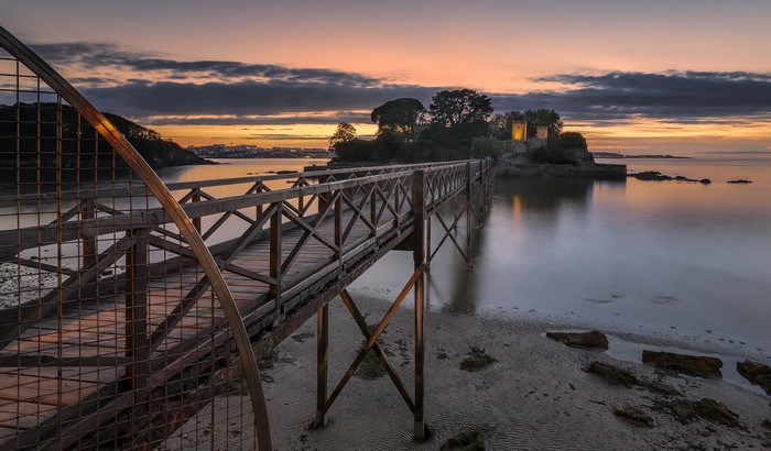 Wooden bridge leading to a castle on an island at sunset