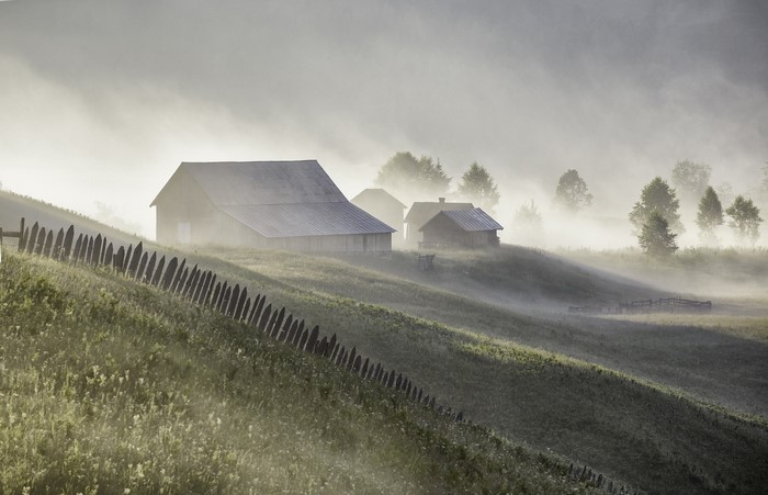 Misty morning on a farm with barns and fence