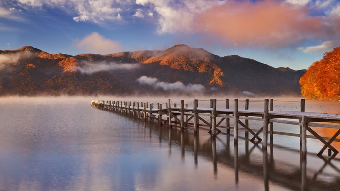 Wooden pier on a misty lake with autumn mountains