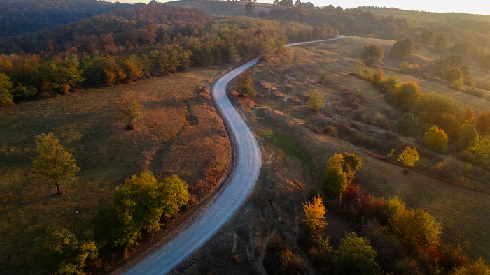 Aerial view of a winding road through autumn hills in Romania at sunrise