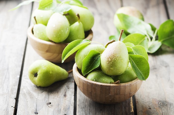 Green pears in wooden bowls on rustic table