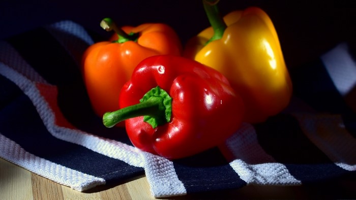 Three colorful bell peppers on a striped cloth