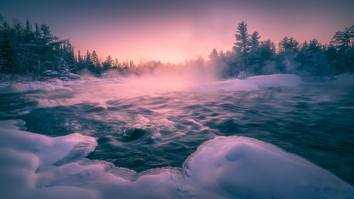 Misty river flowing through a snowy forest at sunrise