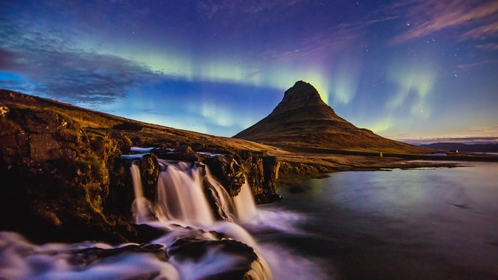 Waterfall and Kirkjufell mountain under aurorae in Iceland