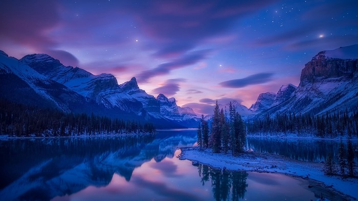 Snowy mountains and lake at twilight with stars
