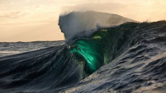 A powerful wave glows green as it crests