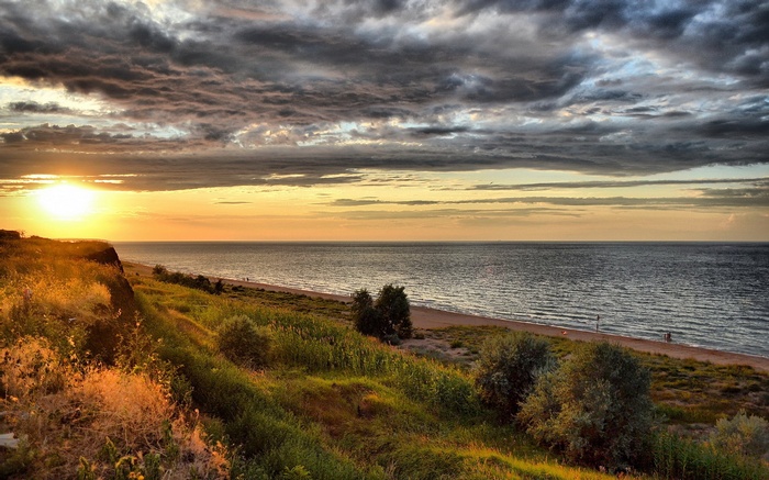 Sunset over the sea with dramatic clouds and grassy cliff