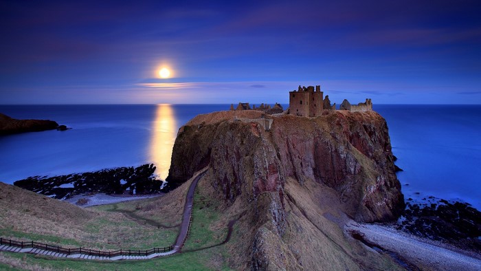 Dunnottar Castle ruins on a cliff by the sea under moonlight