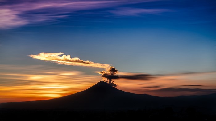 Volcano erupting smoke at sunset with colorful clouds