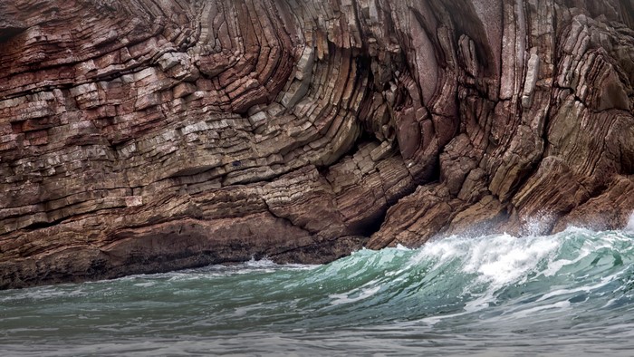 Waves crashing against layered rock formations in Spain