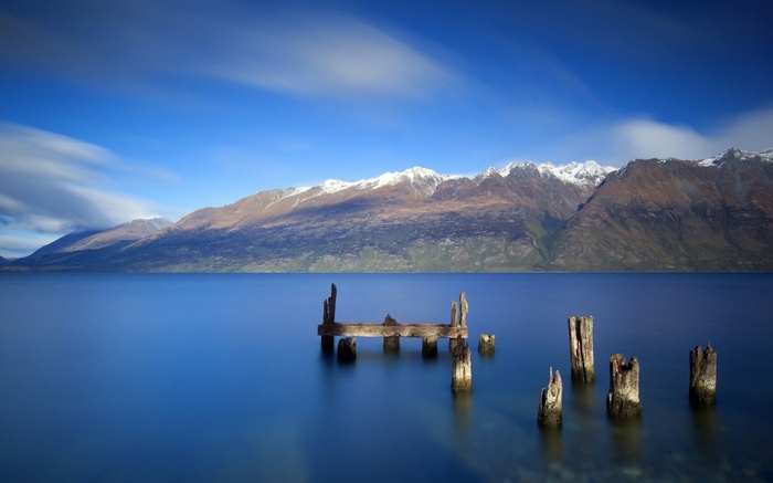 Wooden pier remnants in a calm lake with snow-capped mountains