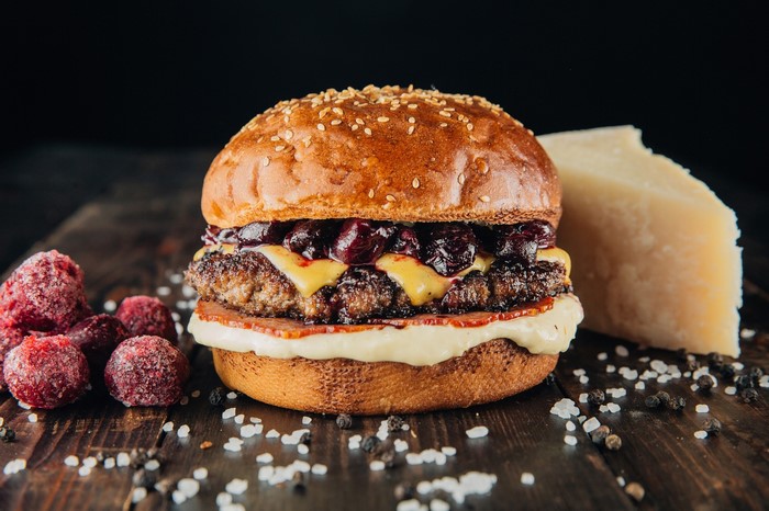 Burger with berries, cheese, and bacon on a wooden table