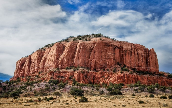 Red rock mountain with sparse vegetation under a cloudy sky