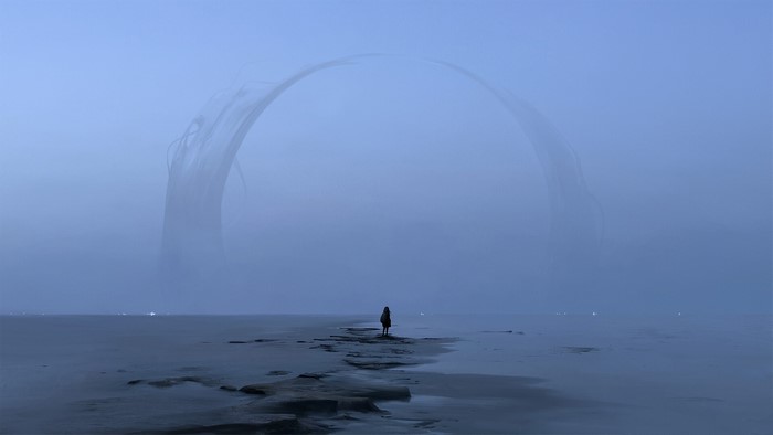 A person stands on a beach looking at a foggy arch