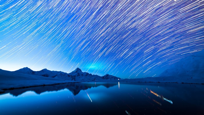 Star trails over snow-capped mountains and a reflective lake