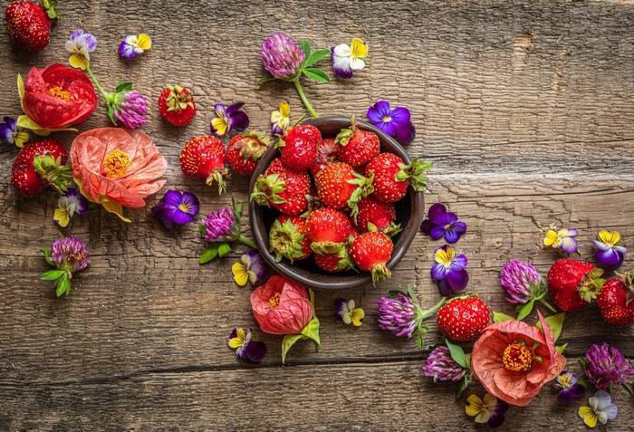 Strawberries and colorful flowers on a wooden table