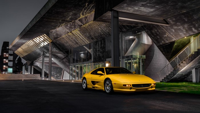 Yellow Ferrari F355 parked at modern building at night
