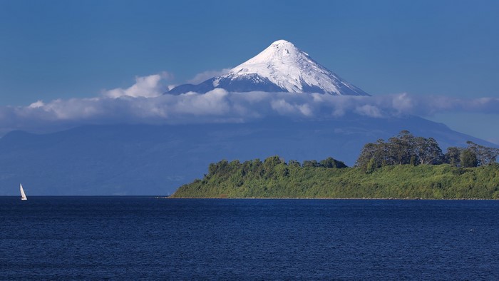 Snowy volcano over a lake with a sailboat