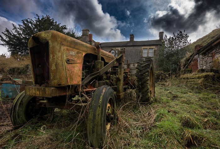 Old rusty tractor in front of a stone house