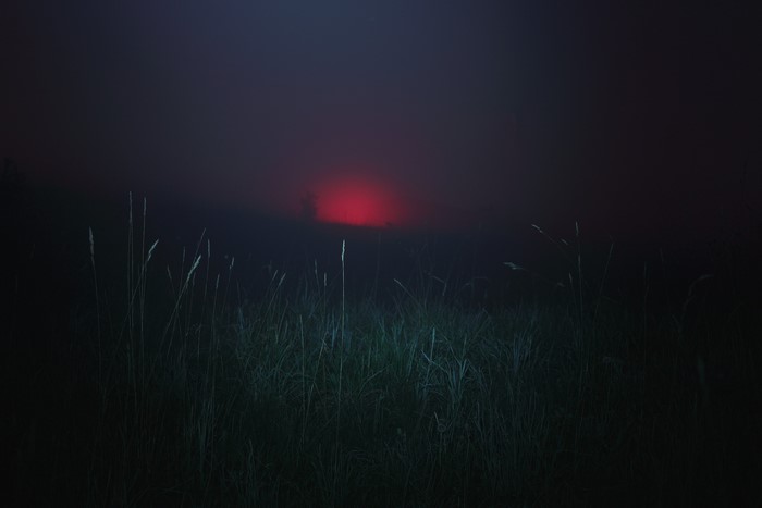 Red sun obscured by mist over a grassy field