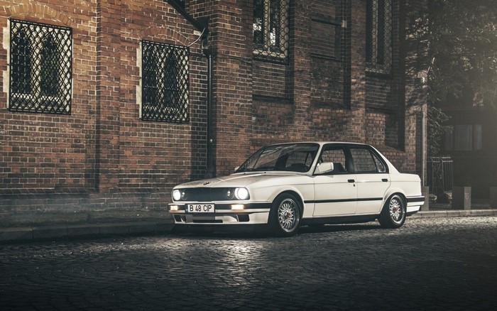 White BMW E30 Sedan parked on cobblestone street