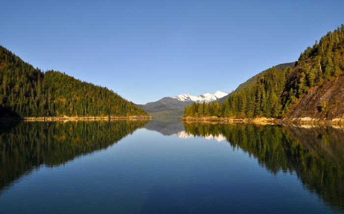 Calm lake reflecting forested mountains and snow-capped peaks