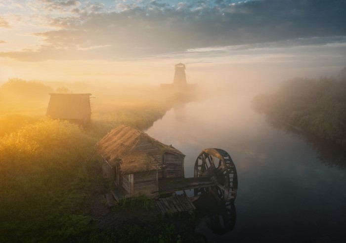 Old mill with water wheel on a misty river at sunrise