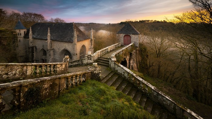 Stone chapel and walkway on a misty hillside at sunrise