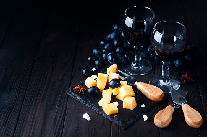 Red wine with cheese and grapes on a dark wooden table