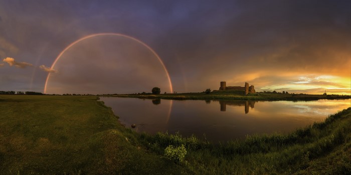 Rainbow over river and castle ruins at sunset
