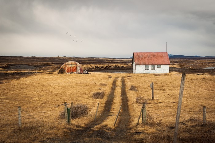 Rural house and barn with dirt road in overcast landscape