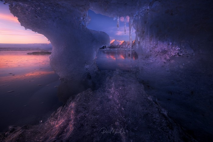 Ice cave at sunset with mountains and ocean