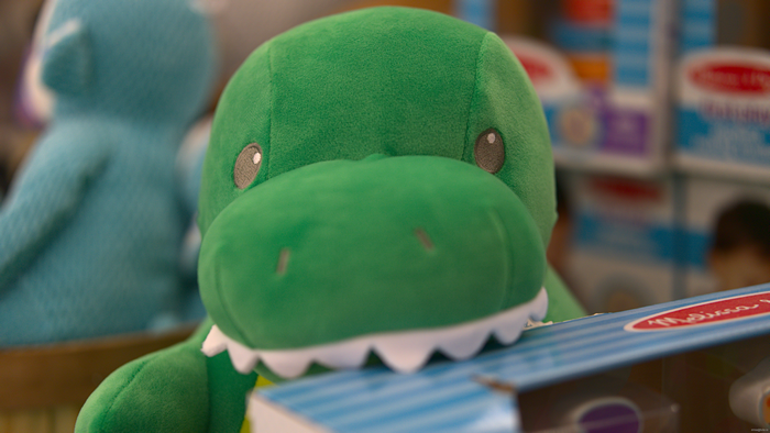 Green dinosaur plush toy in front of blue plush toy