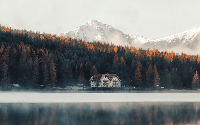 House by a lake with autumn forest and snowy mountains