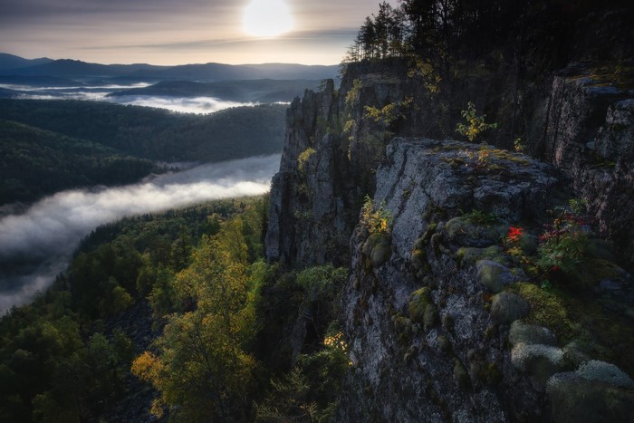 Misty mountain landscape with sun and cliff