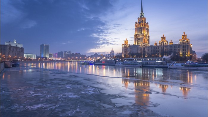 Moscow cityscape with frozen river and illuminated buildings at dusk
