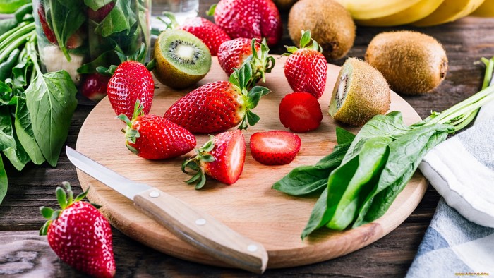 Strawberries, kiwis, bananas, and spinach on a cutting board