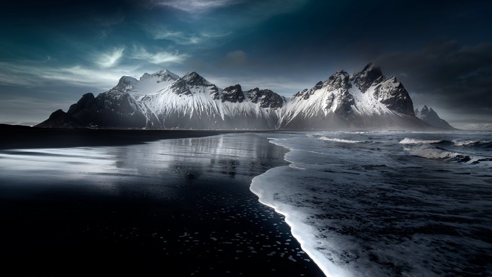 Snowy mountains on a black sand beach with ocean waves
