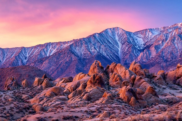 Rocky desert landscape with snow-capped mountains at sunset