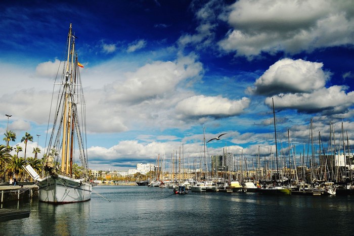 Sailboats docked in Barcelona harbor under a cloudy sky