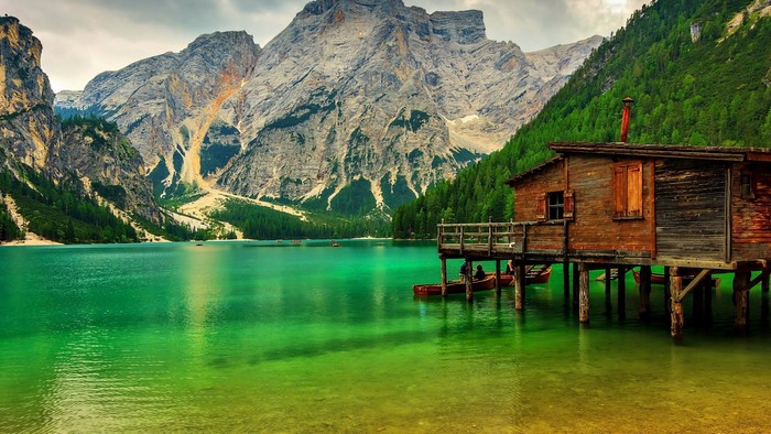 Wooden cabin on stilts by a turquoise lake with mountains