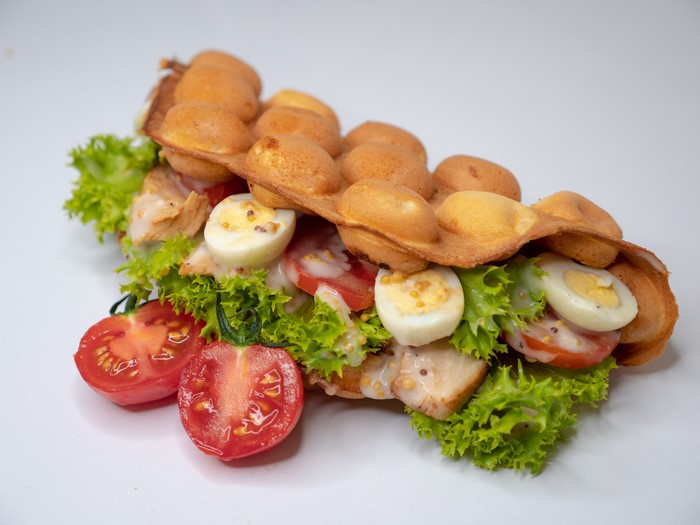 Bubble waffle sandwich with chicken, eggs, tomatoes, and lettuce
