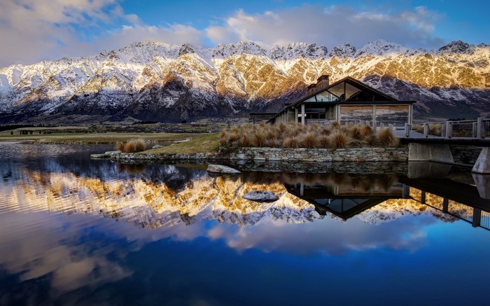 Modern house reflected in a lake with snow-capped mountains
