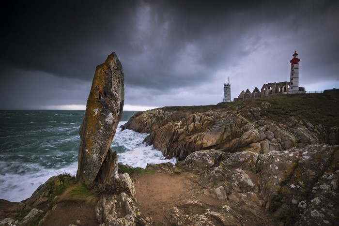Rocky coast with lighthouse and ruins under stormy sky