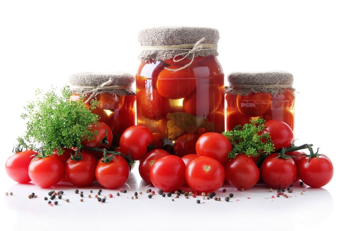 Jars of preserved tomatoes with fresh tomatoes and herbs