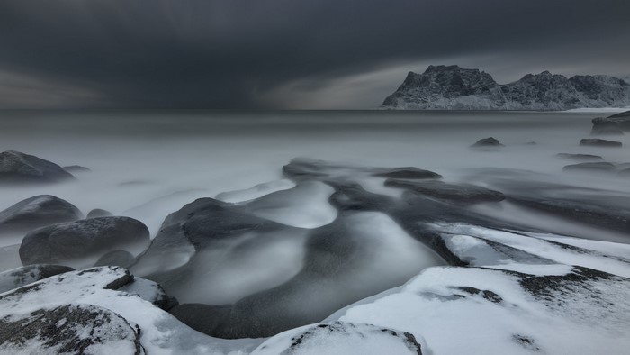 Snowy beach with rocks and mountains in Norway