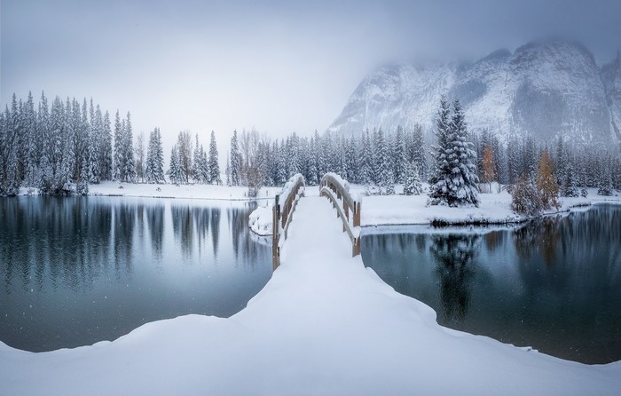 Snowy bridge over a lake with pine trees and mountains