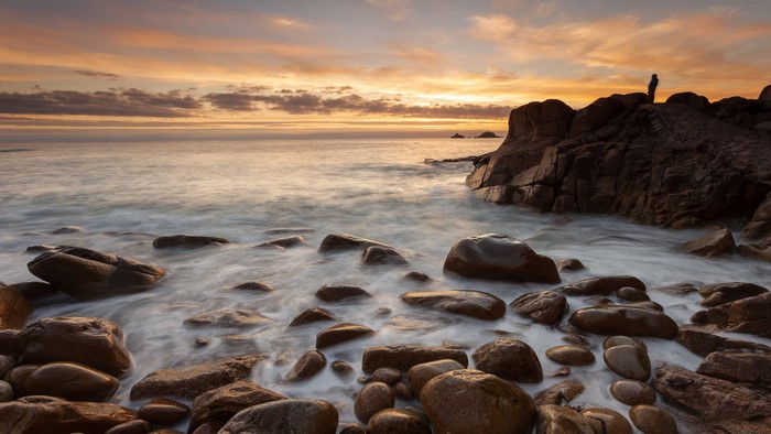 Silhouette of a person on rocks at sunset by the sea